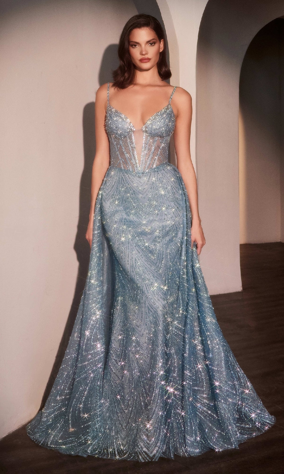 A woman poses against a neutral background, wearing the Ladivine C167 Deep V-Neck Long Glitter Prom Dress—a shimmering light blue formal gown with thin straps, a sheer beaded bodice, mermaid skirt, and intricate sparkling patterns.